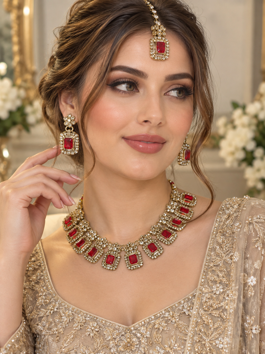 (J2)  Elegant gold-red toned earrings, tikka, and necklace set featuring teardrop-shaped stones surrounded by sparkling crystals