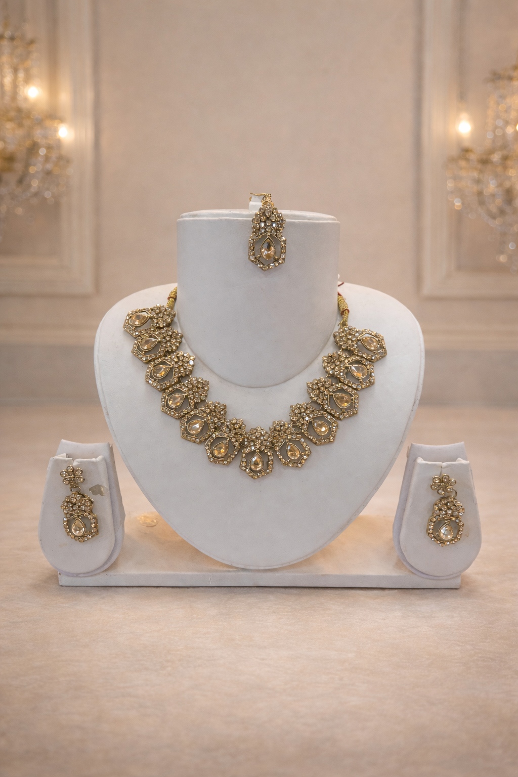 Elegant gold-toned earrings, tikka, and necklace set featuring teardrop-shaped stones surrounded by sparkling crystals.